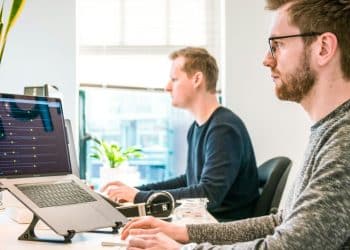 man sitting on chair wearing gray crew-neck long-sleeved shirt using Apple Magic Keyboard