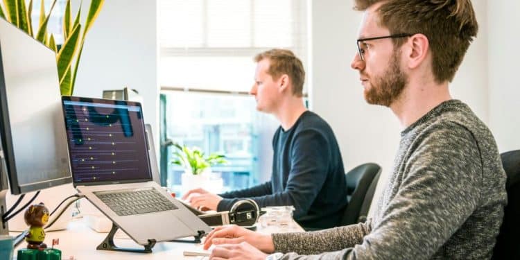 man sitting on chair wearing gray crew-neck long-sleeved shirt using Apple Magic Keyboard