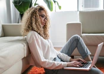 woman sitting on floor and leaning on couch using laptop